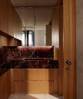 Modern bathroom fitted with red marble countertops, with prominent white veining, and wooden units that surround