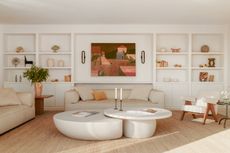 White living room with jute rug, built-in joinery across the length of a wall, cream sofas and curved two-piece coffee table
