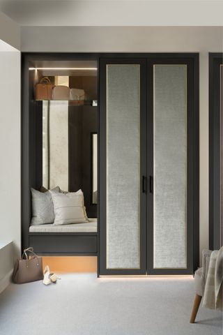 A gray and black built-in closet with a small seat and closet lighting