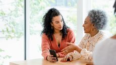 A younger woman and an older woman have a discussion while sitting at a table.