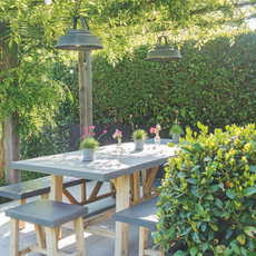 A mordne patio surrounded by a large hedgerow