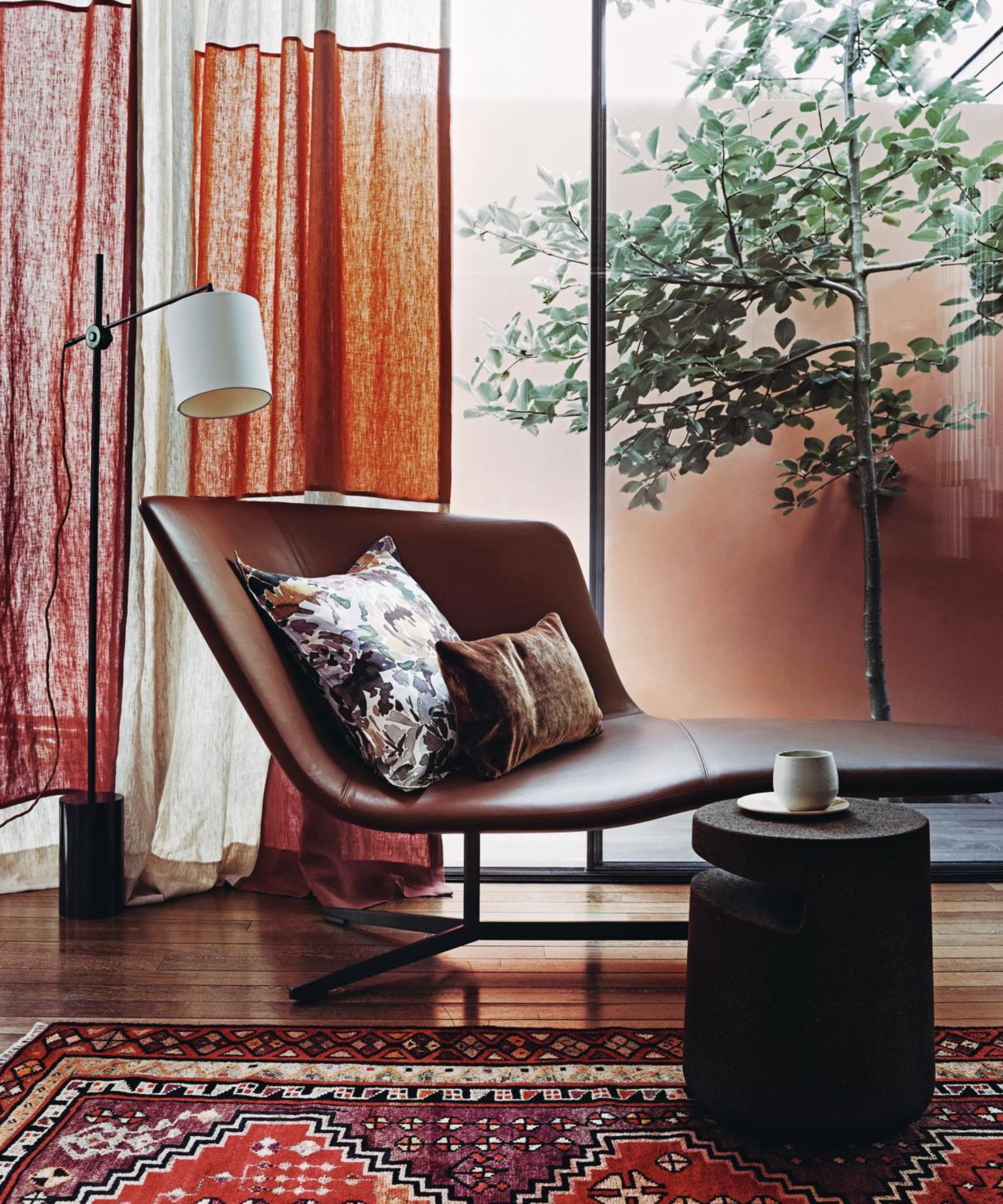 tan leather chair with cushions on and a reading light above it, by a window with a tree outside, in a red and orange themed room
