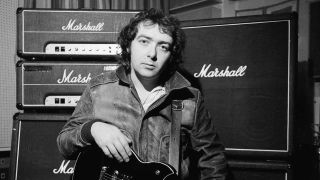 Bernie Marsden holding a guitar, standing in front of some amplifiers