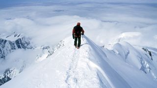 Climber on steep, exposed snowy summit of Europe's tallest peak, Mt Blanc