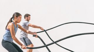 A man and woman exercising with battle ropes outside