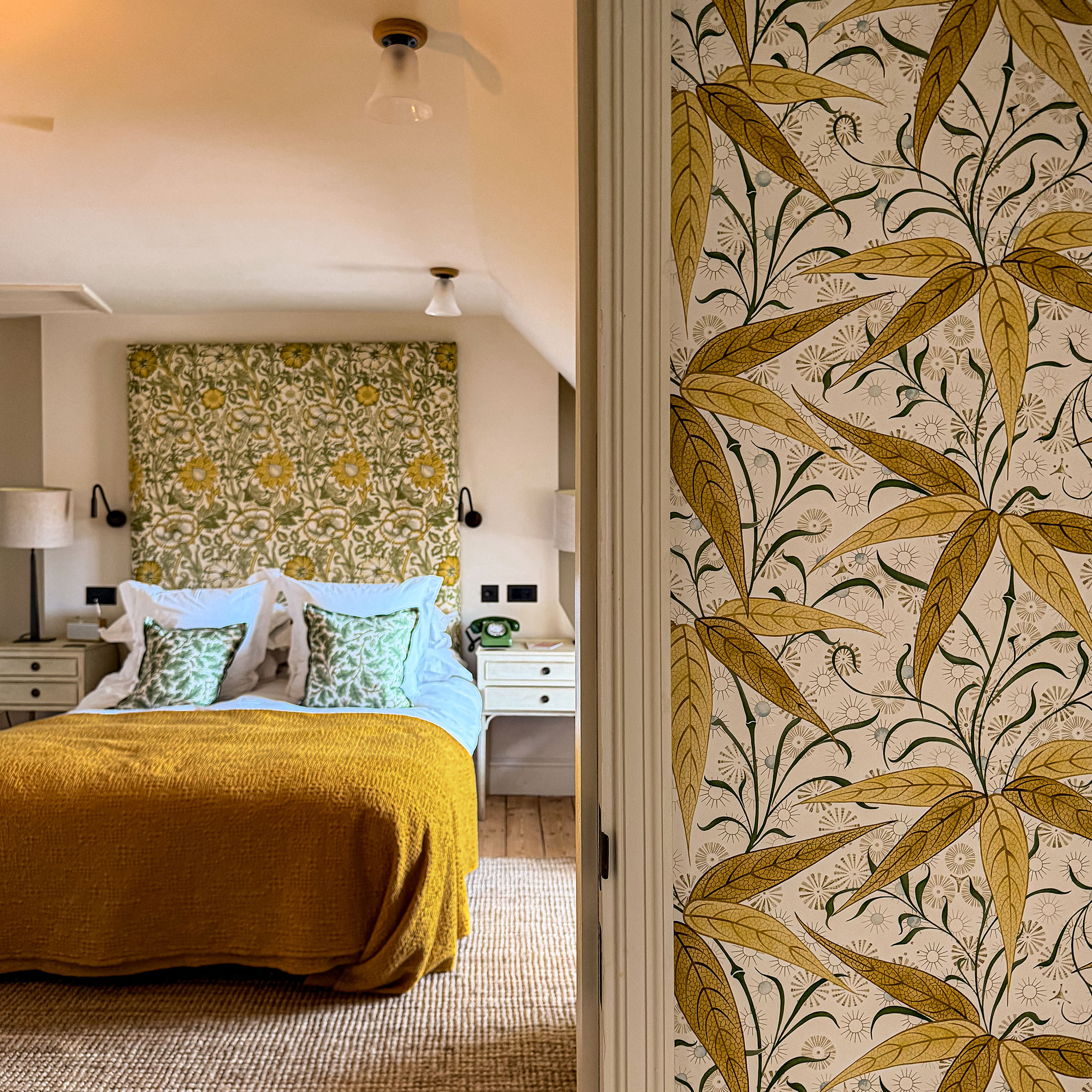 Bedroom with yellow patterned feature wall behind bed with ochre throw