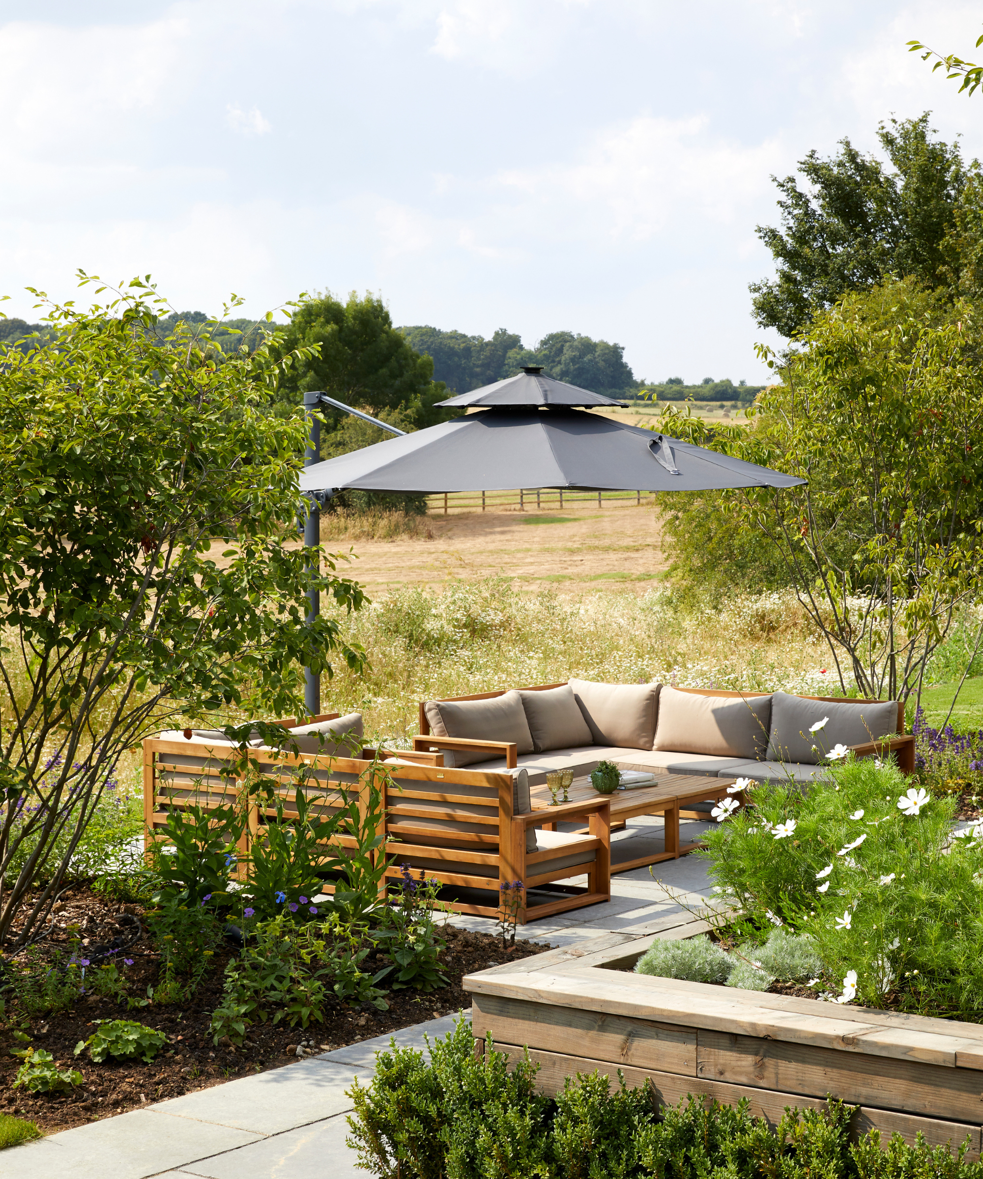a backyard with a large umbrella, a large sofa, and a field that stretches beyond