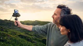 two people hold up to selfie with the lumix ZS99 while it is on a selfie stick