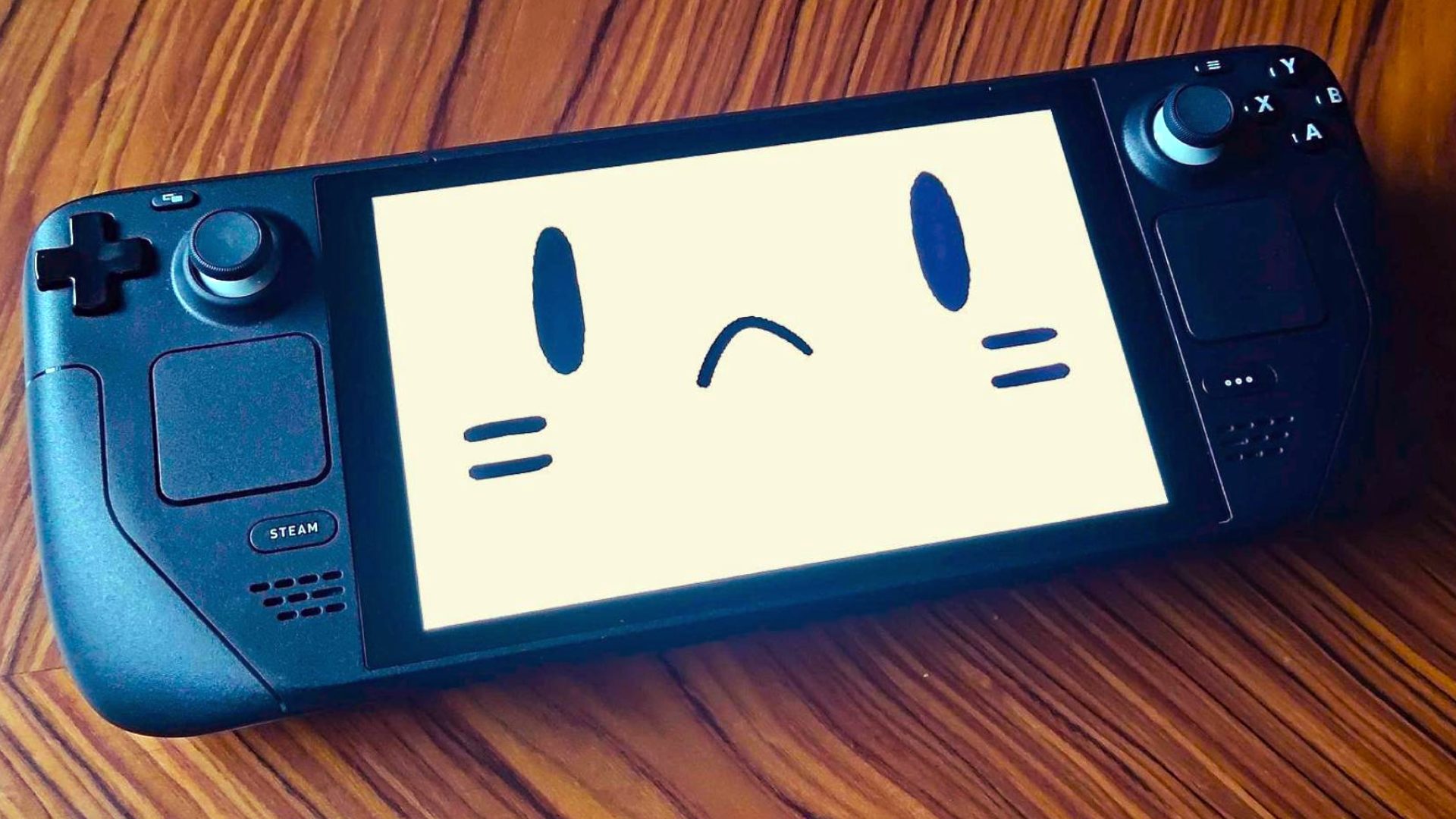 Steam Deck LCD on woodgrain table with sad face on screen.