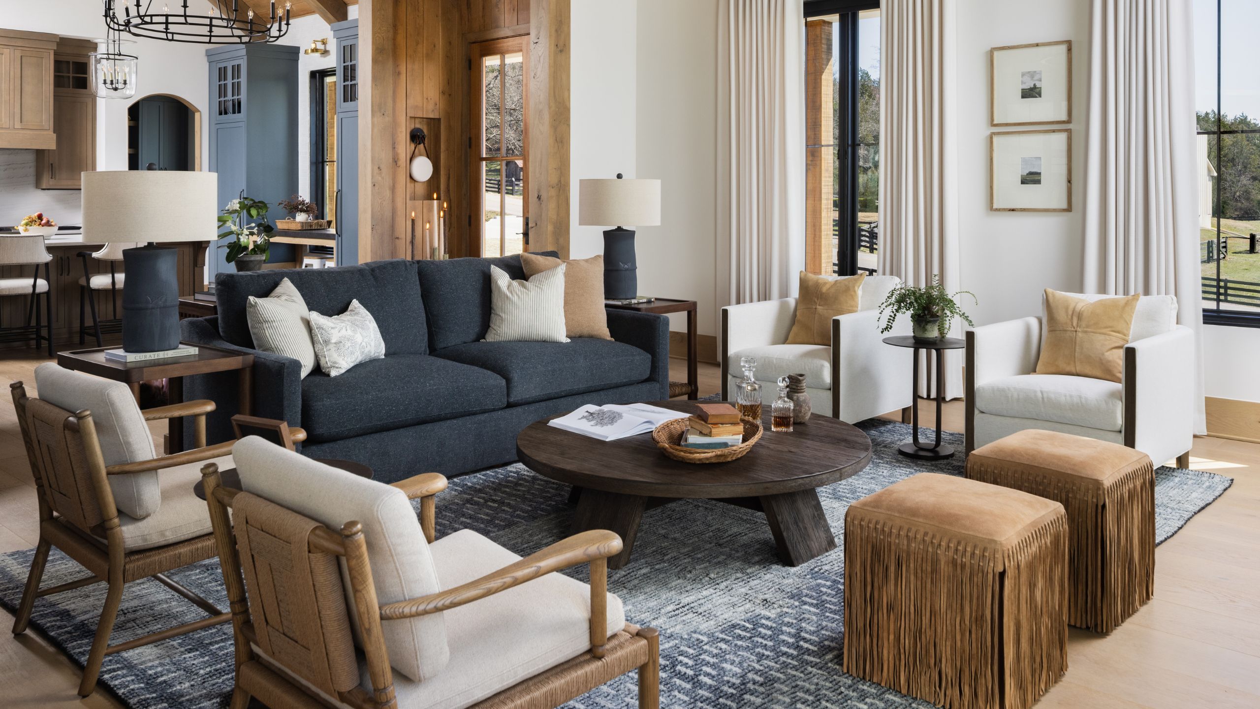 Luxurious rustic living room with vaulted wood ceiling, dark blue sofa, round wooden coffee table, white armchairs, and round wrought-iron chandeliers.