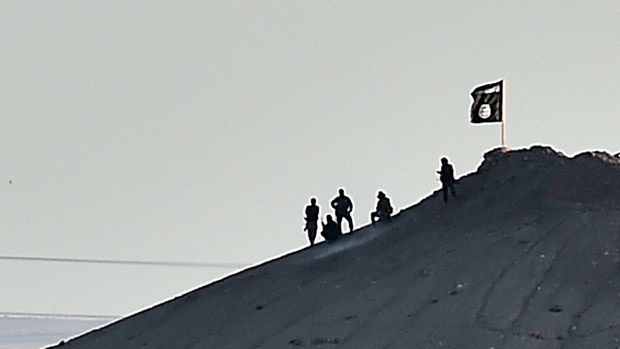 Islamic State (IS) militants stand next to an IS flag atop a hill in the Syrian town of Ain al-Arab, known as Kobane