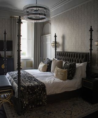 elegant bedroom with ivory wallpaper, black four poster bed, monochromatic throw and bed pillows, rug, modern circular chandelier, original features