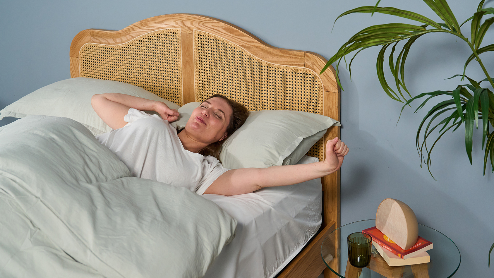 A woman lies in bed and stretches her arms like she's feeling sleepy