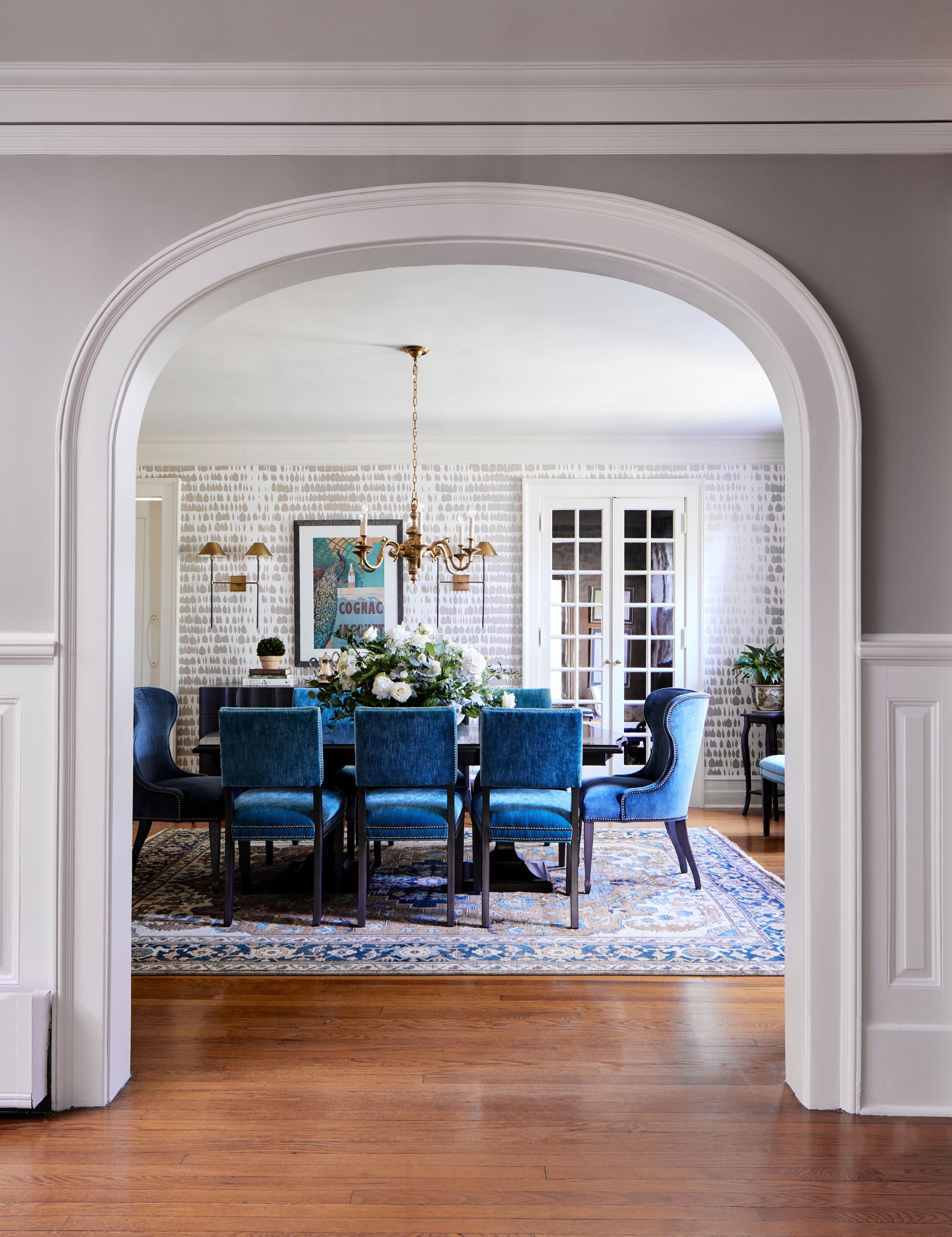 View through an arch into a dining room with a large area rug and blue velvet dining chairs