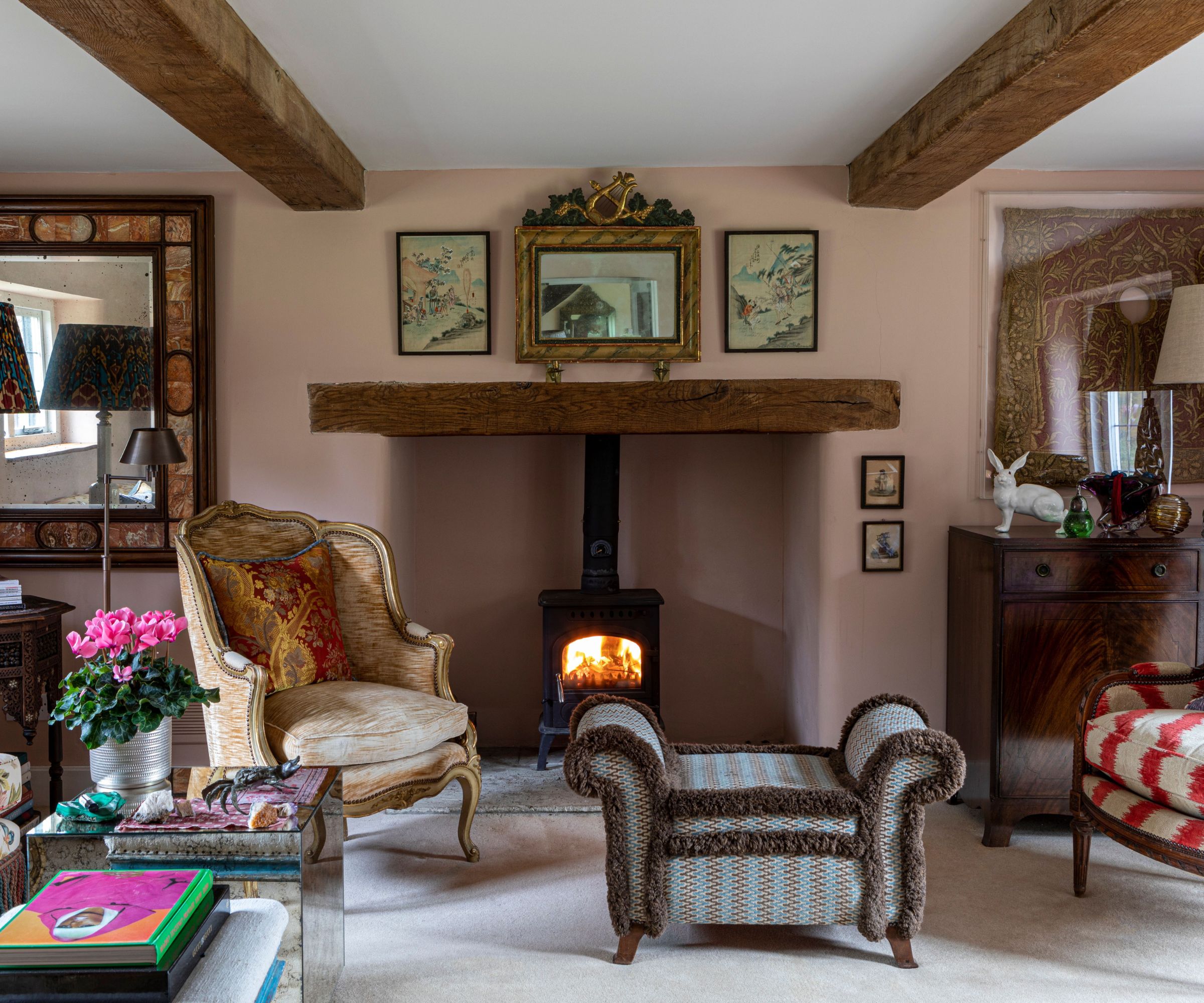 pink traditional vintage style living room with beamed ceiling, log burner fire, antique furniture and large artwork