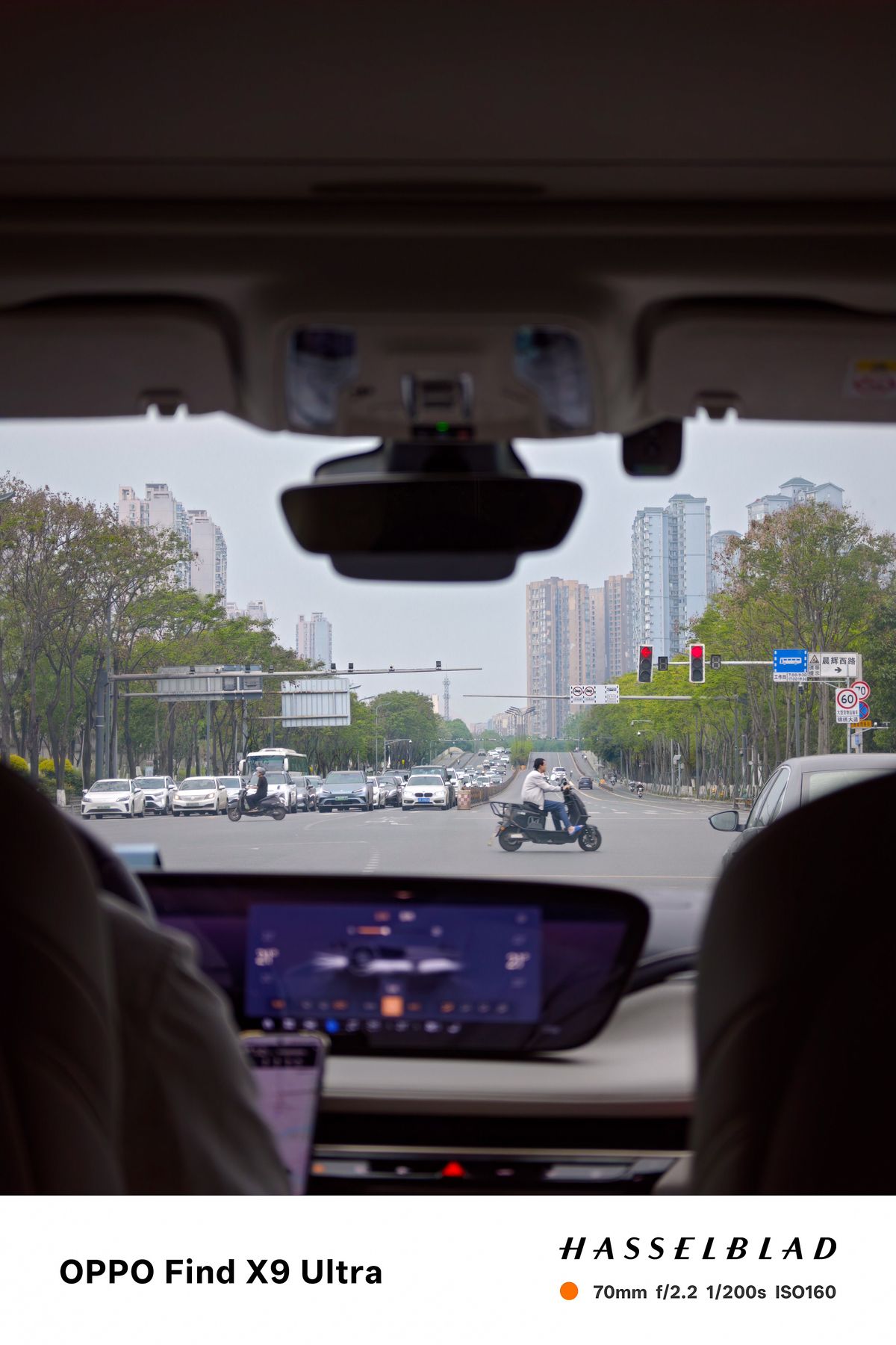 View through a car windshield at a broad city intersection with scooters and traffic
