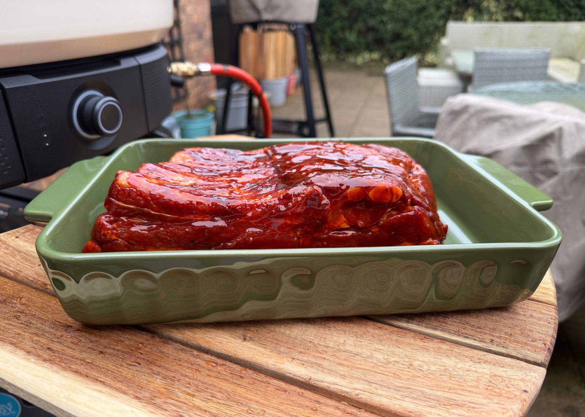 A close-up of a green dish containing ribs on the shelf of a Gozney Dome XL Gen 2 outdoor pizza oven with another pizza oven and table in the background
