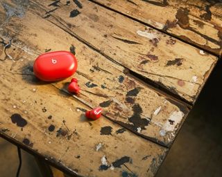 Beats Studio Buds in red with charging case on weathered wooden table