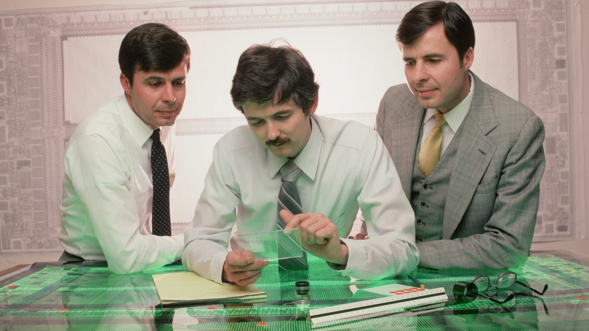 Twins Joe and Ward Parkinson, the founders of Micron Technology, Inc., examine a computer chip with designer Doug Pitman at their manufacturing company in Boise, Idaho. The chip will be a 64K RAM memory chip.