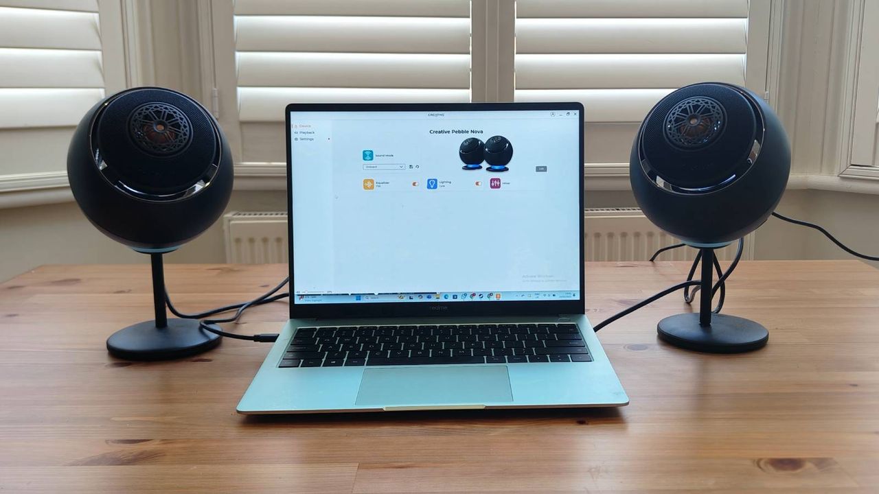 The Creative Pebble Nova on a brown table, connected to a green laptop.
