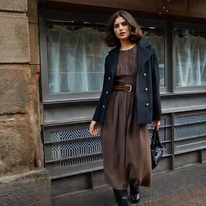 Model wearing a brown dress and belt with a black collared jacket sold at Oasis