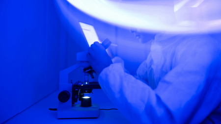 A scientists looks down a microscope.