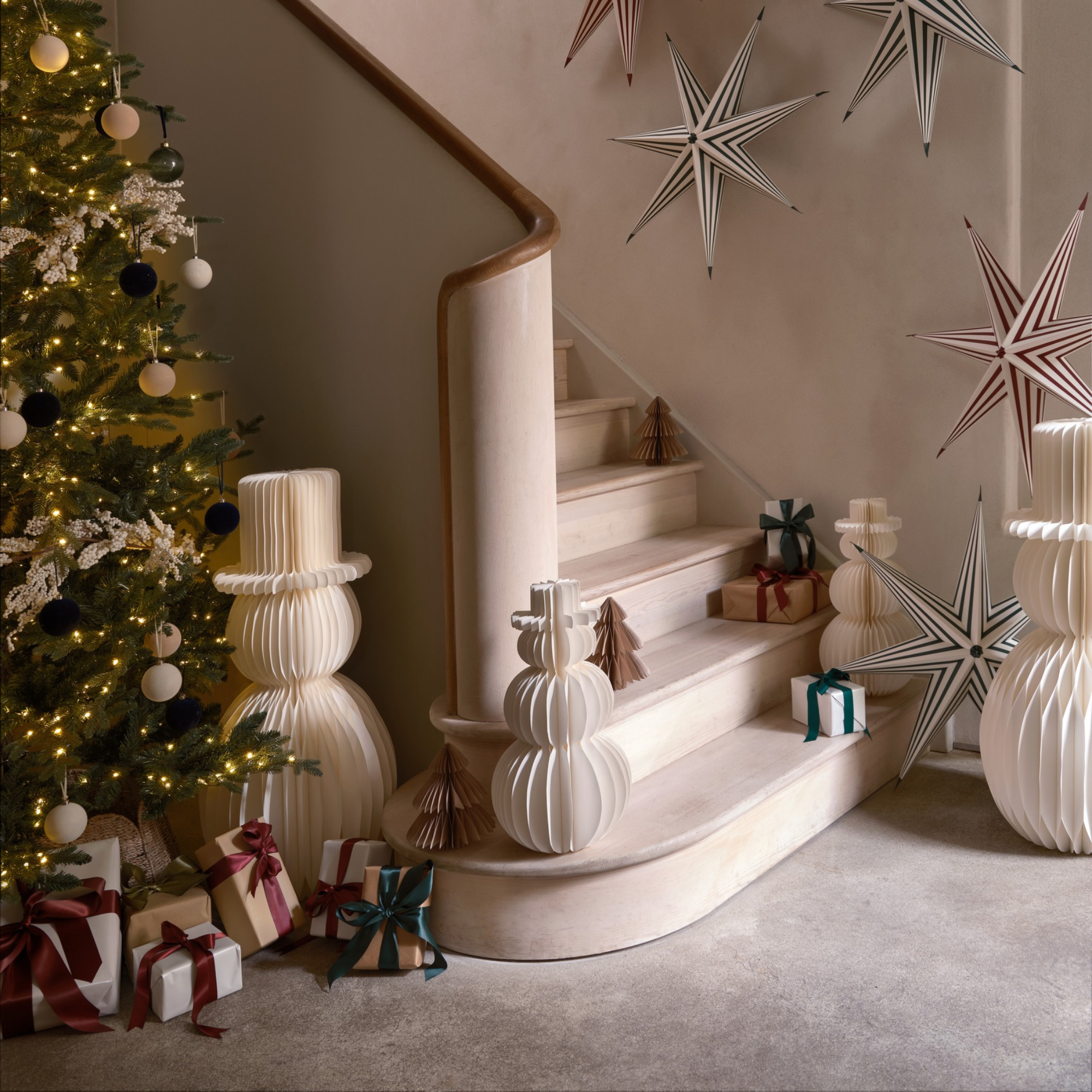 Habitat paper snowman next to a christmas tree in a hallway. Paper stars are on the wall and there are loads of wrapped presents.
