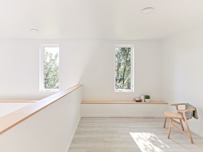 Hem House by Future Firm. A loft area with a wooden chair, a wall bench with plants on and rectangular vertical windows.