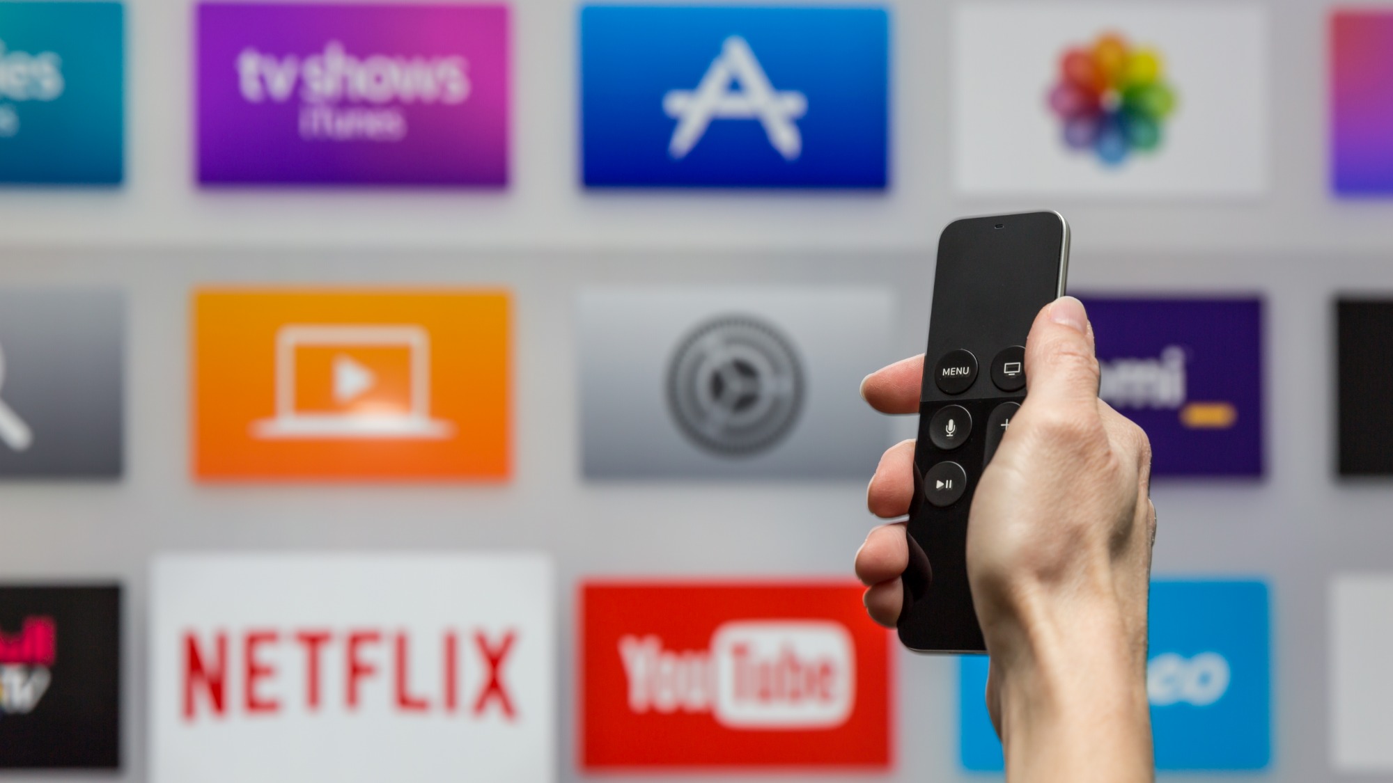 Human hand holding TV remote browsing streaming service selections, including Netflix