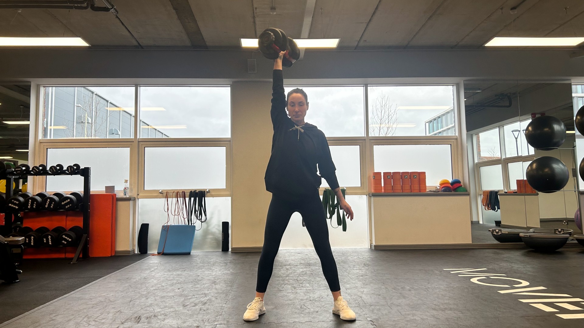 Auteur Sam voert een dumbbell snatch uit in de sportschool met een Bowflex SelectTech 552i verstelbare dumbbell die boven zijn hoofd in de lucht wordt gehouden met opgeheven rechterarm