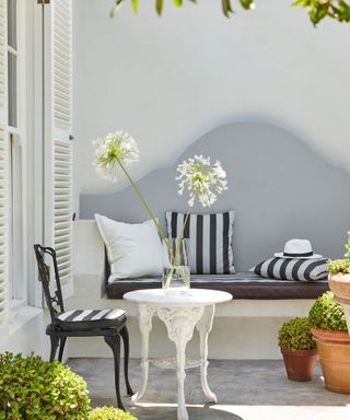 front yard with white walls, white table with black chair, bench seating against wall