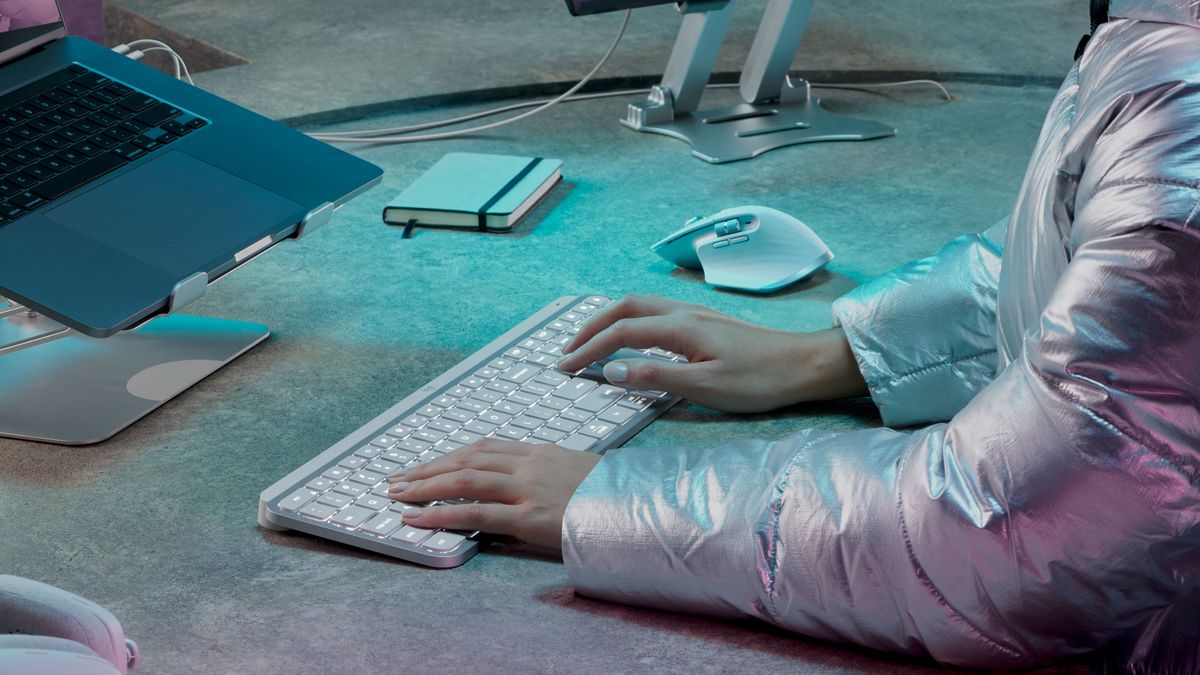 The Logitech MX Keys S keyboard in pale grey colorway sitting on a desk and being used by a pair of hands.