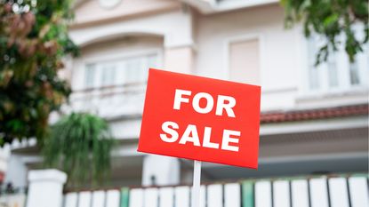 Blurred exterior of home with red For Sale sign in center and focus