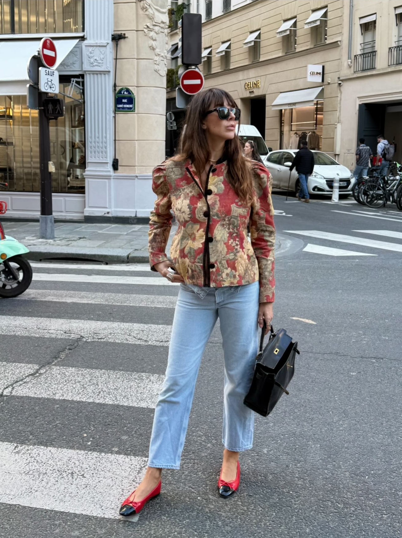 An image of an influencer in Paris wearing a tapestry jacket with light-wash jeans and red ballet flats with black toe caps carrying an open handbag