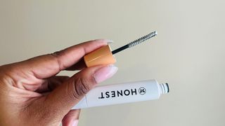 A person holding an opened white mascara tube with the primer end, for the Honest Beauty Extreme Length + Lash Primer review.