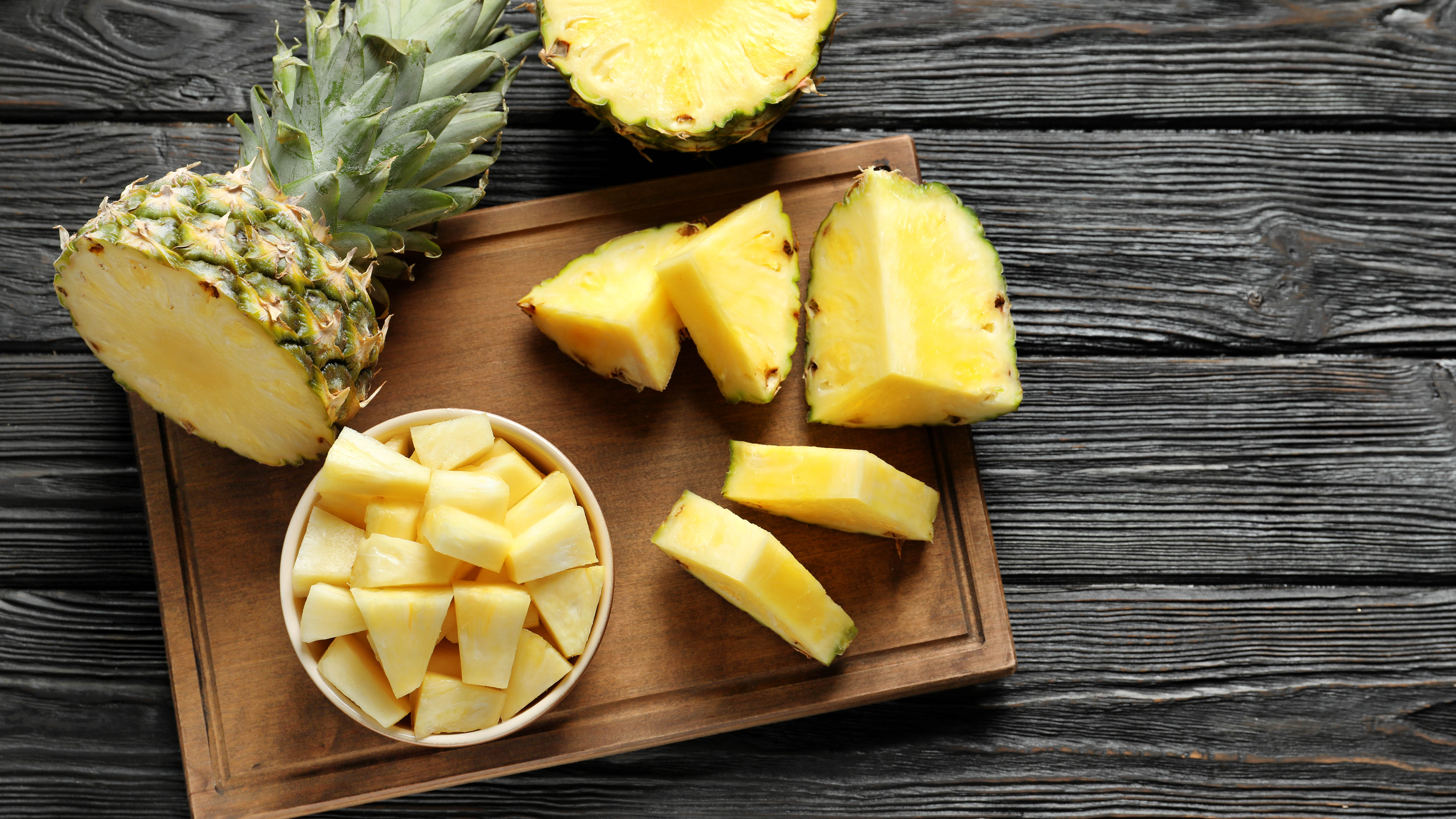 A pineapple cut into chunks in a bowl on a cutting board