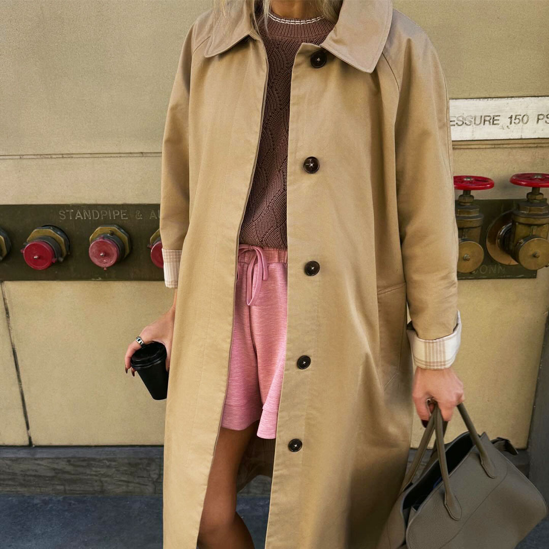 a woman wearing a trench coat, pink shorts, and loafers