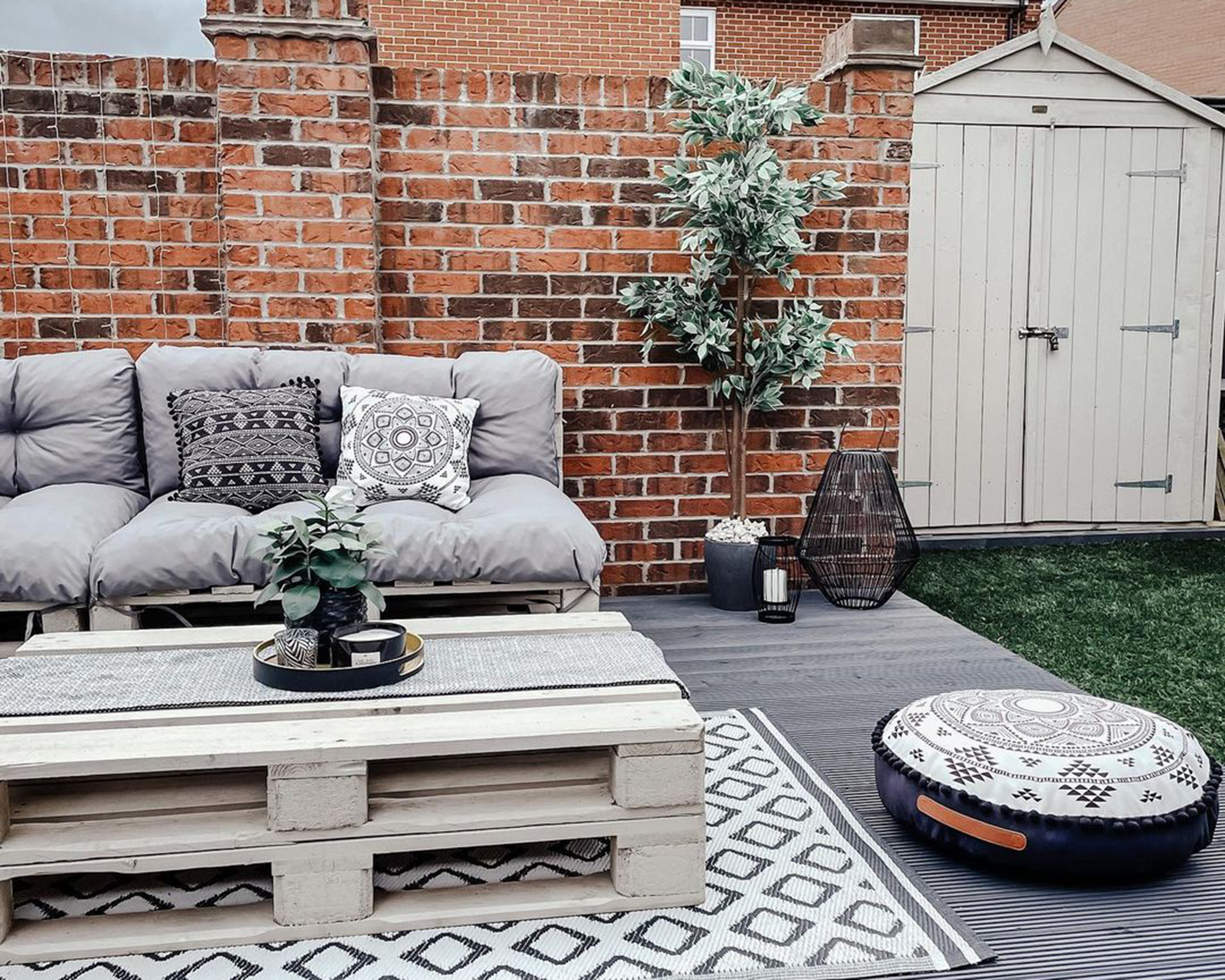 A Scandinavian inspired deck idea with cream painted pallet furniture, cushions and faux grass with shed in background