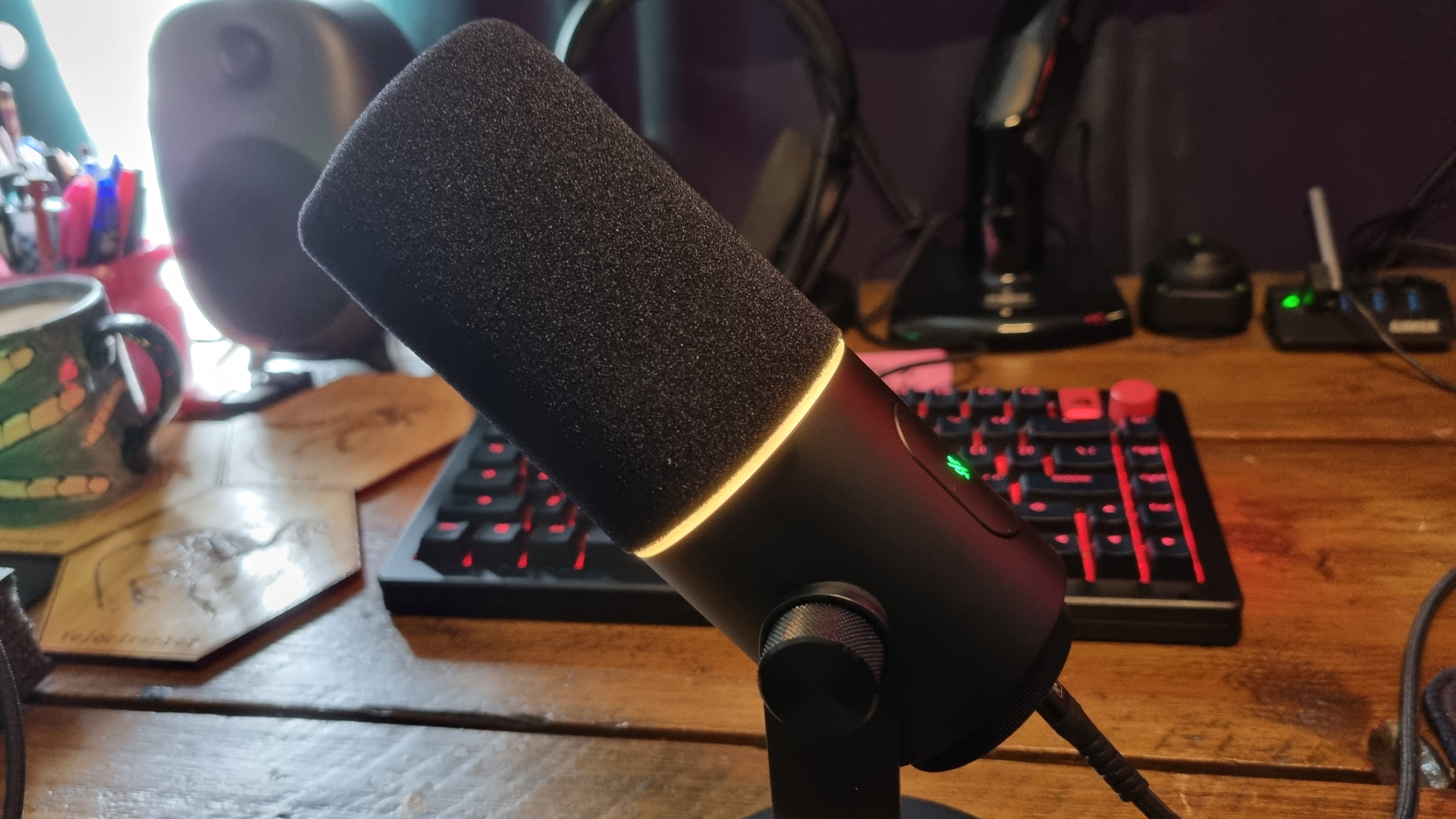 A Razer Seiren V3 Pro microphone in front of a gaming keyboard, with its RGB ring lit in yellow