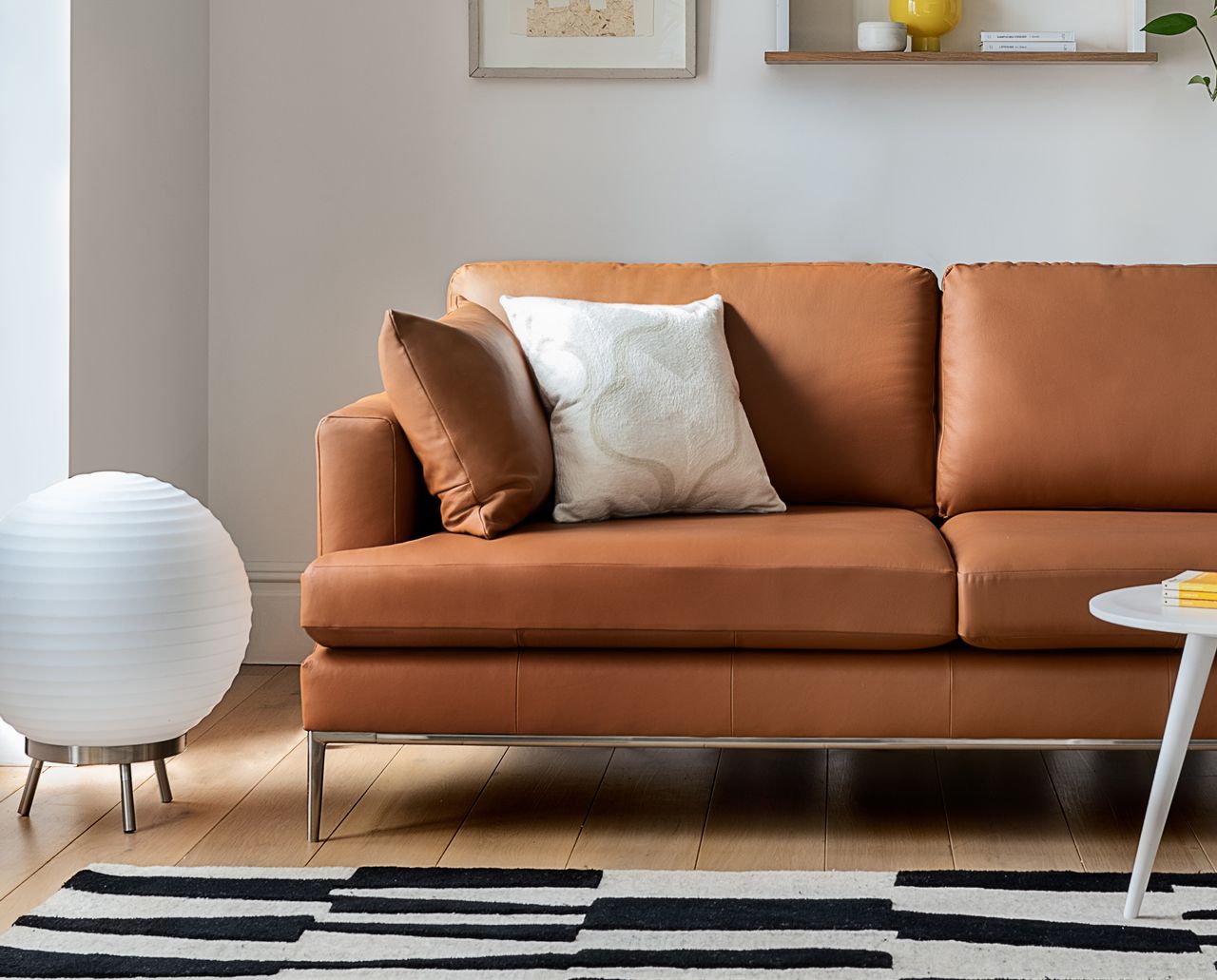 A living room with a leather sofa, globe paper floor lamp, and a black and white geometric rug