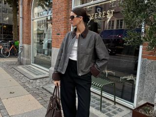 Fashion influencer @maryljean in Copenhagen wearing an on-trend outfit for spring 2025 with a contrast collar jacket, Miu Miu bag and sunglasses, relaxed trousers, white tee, and suede boat shoes.