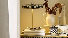 Mackenzie-Childs Courtly Check portable lamp styled alongside tableware from the collection, including a lidded ceramic vessel and various trinket trays.