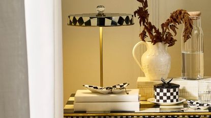 Mackenzie-Childs Courtly Check portable lamp styled alongside tableware from the collection, including a lidded ceramic vessel and various trinket trays.