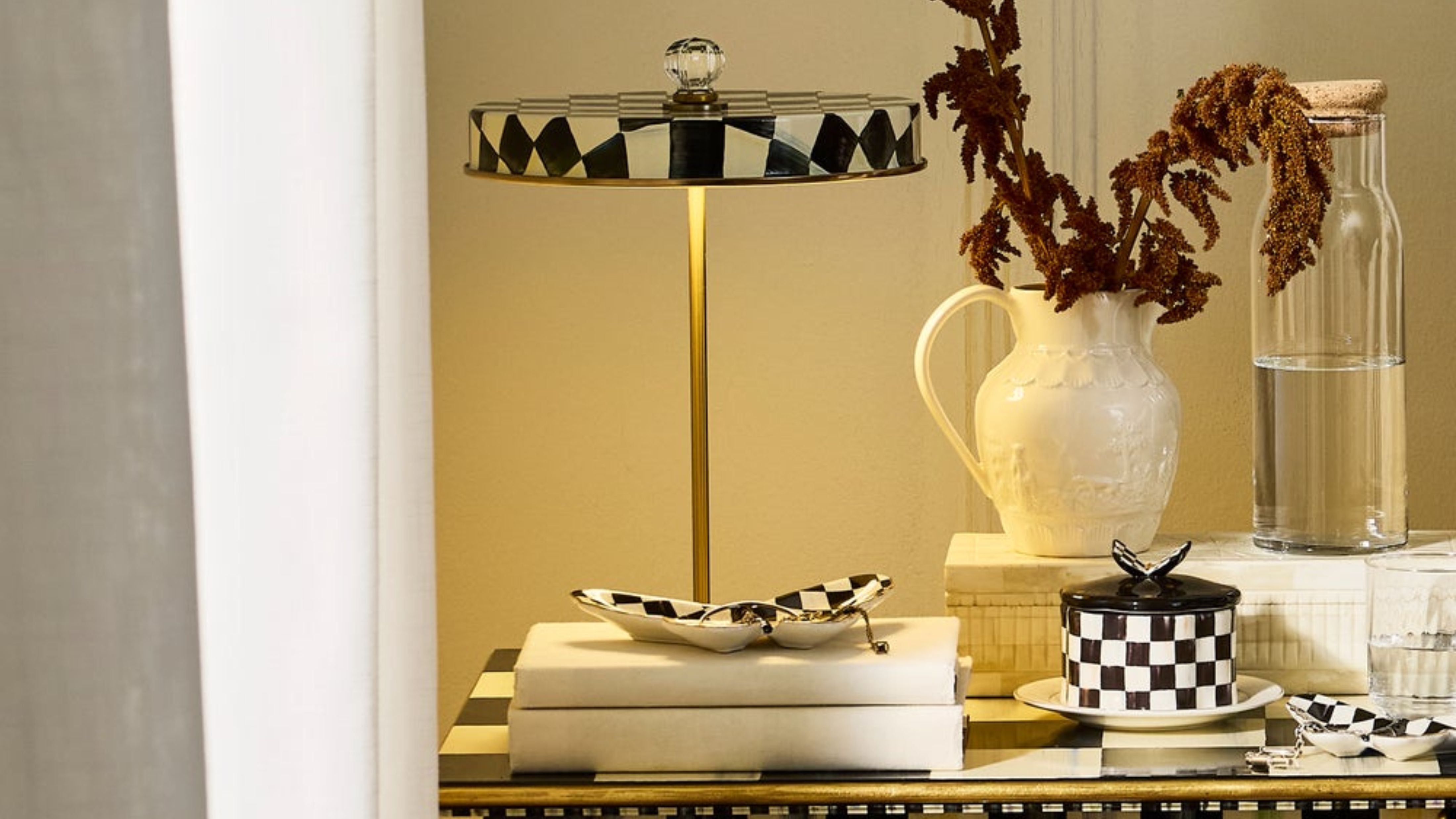 Mackenzie-Childs Courtly Check portable lamp styled alongside tableware from the collection, including a lidded ceramic vessel and various trinket trays.