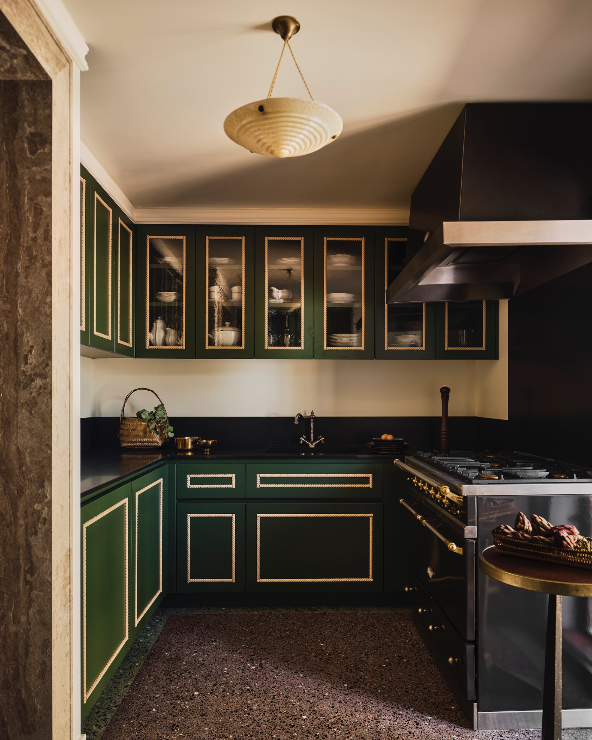 Dark Empire Green lacquered kitchen cabinetry with rope-style moldings, black stone countertops and backsplash, and a Lacanche range.