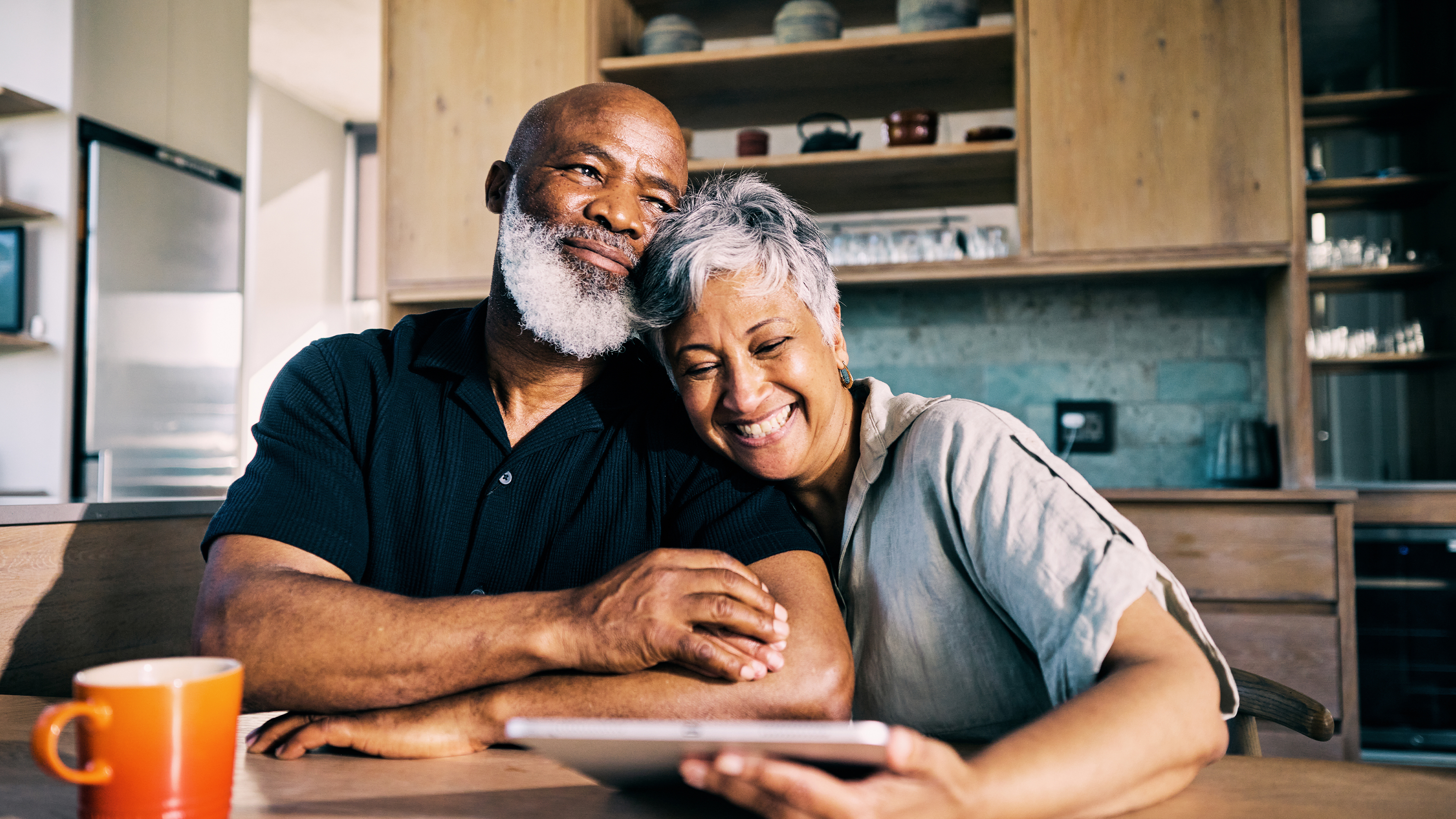 Two people at the kitchen table embracing, smiling toward the camera.