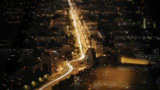Aerial night view of a city, showcasing illuminated streets and buildings, with a blur effect enhancing the ambiance