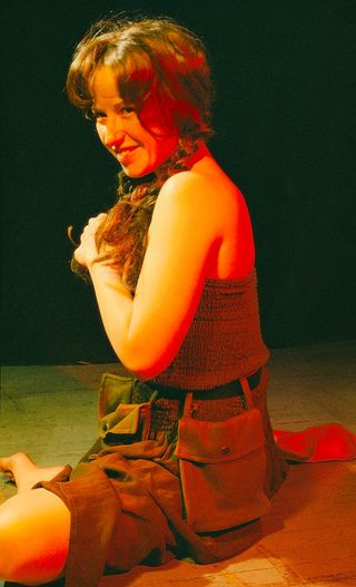 Portrait of a grinning Cindy Sherman, seated on the floor and bathed in red light