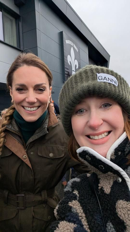 Princess Kate wearing a green coat taking a selfie with a woman wearing a green winter hat and smiling
