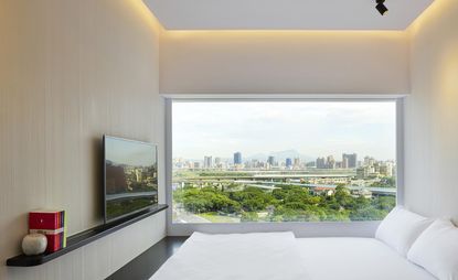 Hotel bedroom with view over city, white linen, black marble floor and TV mounted on wall